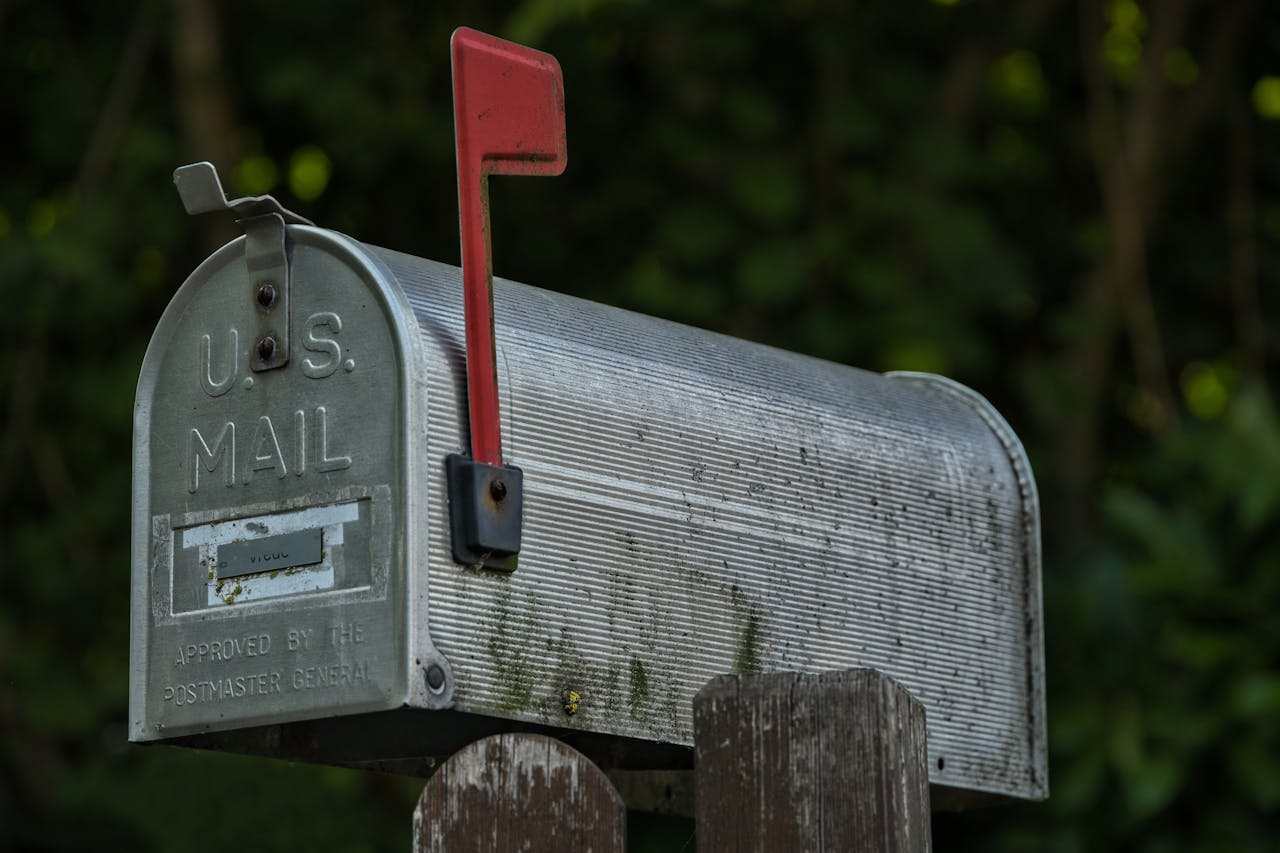home-services-004 A classic U.S. mailbox with a red flag in a green outdoor setting, evoking nostalgia.
