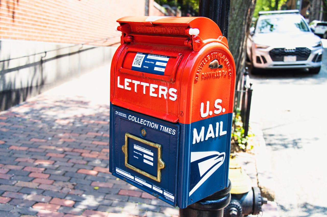 cta-bg Vibrant U.S. mailbox on a city sidewalk with a parked car, conveying a classic urban scene.